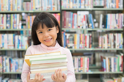 child girl holding a stack of books in the library