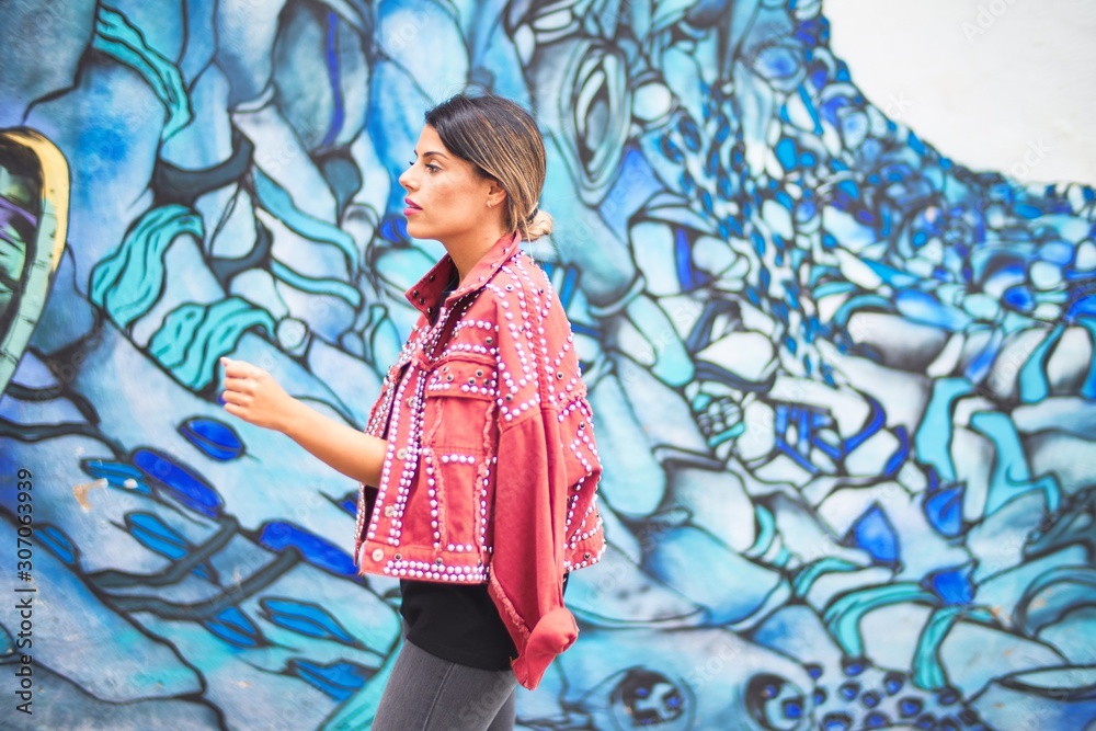 Fototapeta premium Young beautiful girl wearing red jacket standing backwards over colorful wall at the town street