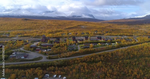 Autumn colors in Abisko town, aerial, reverse, drone shot, of a arctic village, mountains in the background, on a sunny fall day, in Lappland, Norrbotten, North Sweden photo