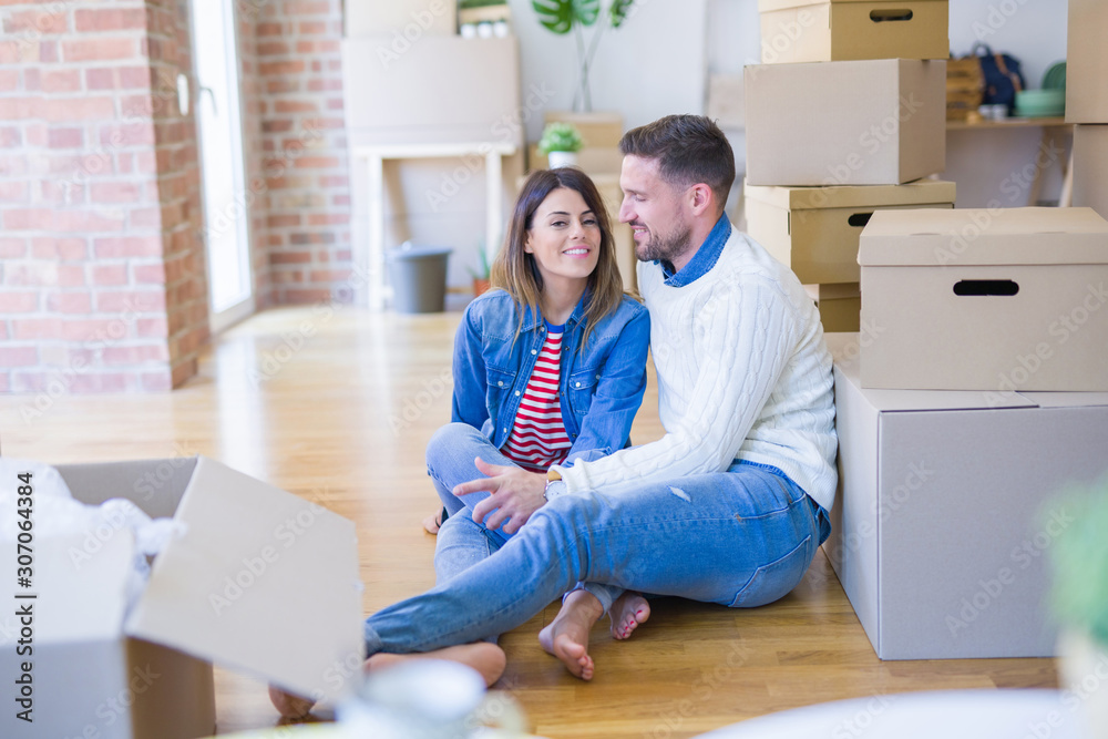 Young beautiful couple sitting on the floor at new home around cardboard boxes Young beautiful couple sitting on the floor at new home around cardboard boxes