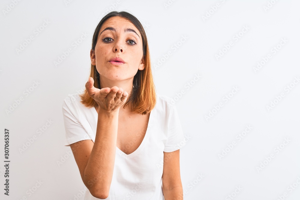 Beautiful redhead woman wearing casual white t-shirt over isolated background looking at the camera blowing a kiss with hand on air being lovely and sexy. Love expression. Beautiful redhead woman wearing casual white t-shirt over isolated background looking at the camera blowing a kiss with hand on air being lovely and sexy. Love expression.