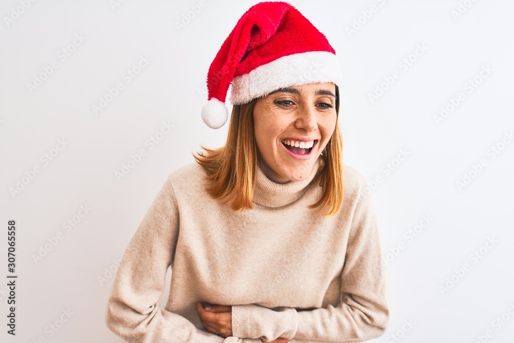 Beautiful redhead woman wearing christmas hat over isolated background smiling and laughing hard out loud because funny crazy joke with hands on body. Beautiful redhead woman wearing christmas hat over isolated background smiling and laughing hard out loud because funny crazy joke with hands on body.