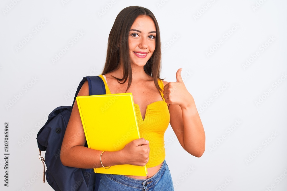 Beautiful student girl wearing backpack holding notebook over isolated white background happy with big smile doing ok sign, thumb up with fingers, excellent sign Beautiful student girl wearing backpack holding notebook over isolated white background happy with big smile doing ok sign, thumb up with fingers, excellent sign
