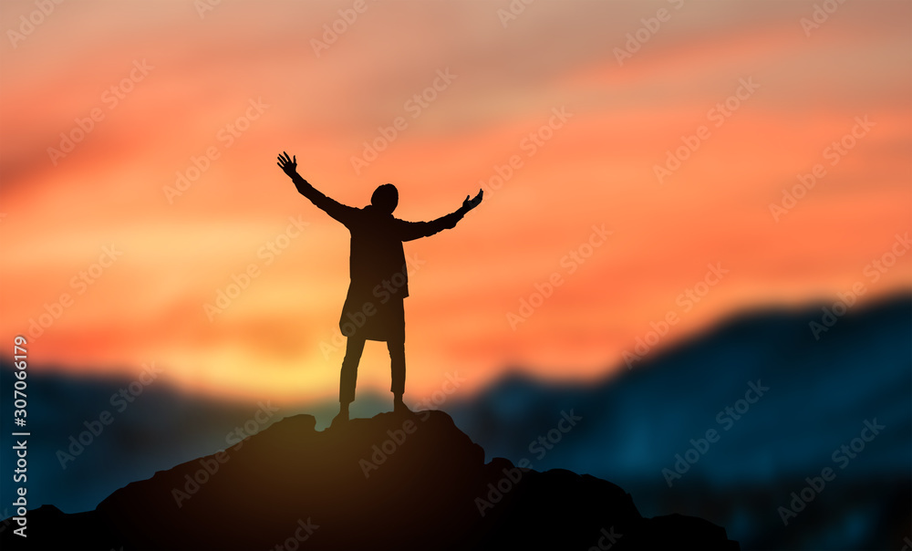 a silhouette man raise hand up on top of mountain with sunset sky and clouds abstract background.