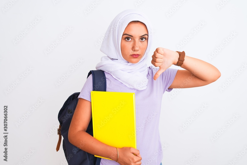 Arab student girl wearing hijab and backpack holding book over isolated white background with angry face, negative sign showing dislike with thumbs down, rejection concept Arab student girl wearing hijab and backpack holding book over isolated white background with angry face, negative sign showing dislike with thumbs down, rejection concept