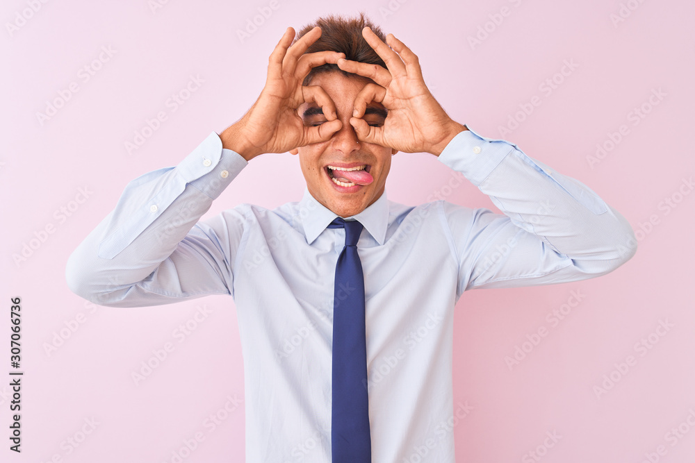 Young handsome businessman wearing shirt and tie standing over isolated pink background doing ok gesture like binoculars sticking tongue out, eyes looking through fingers. Crazy expression. Young handsome businessman wearing shirt and tie standing over isolated pink background doing ok gesture like binoculars sticking tongue out, eyes looking through fingers. Crazy expression.