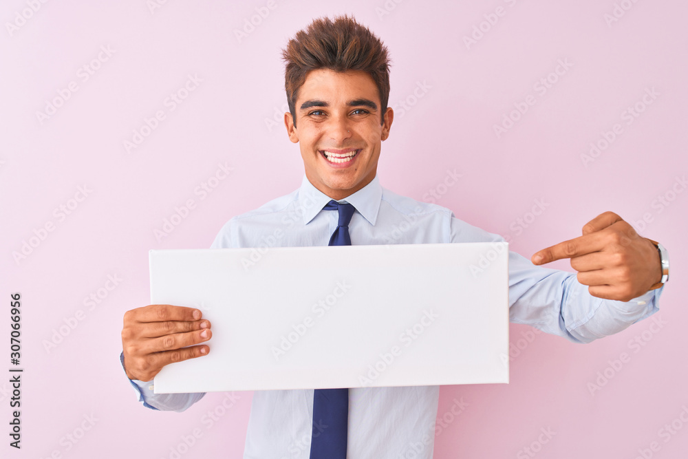 Young handsome businessman holding banner standing over isolated pink background very happy pointing with hand and finger Young handsome businessman holding banner standing over isolated pink background very happy pointing with hand and finger