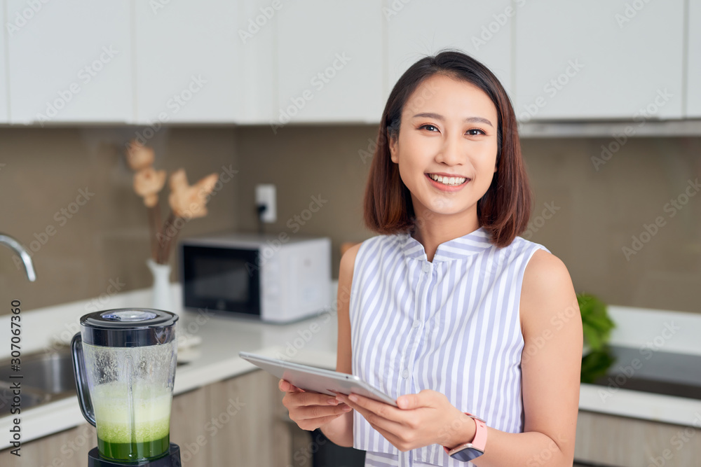 Asian woman using tablet to find recipe making smoothie with fruit and vegetable in kitchen. Asian woman using tablet to find recipe making smoothie with fruit and vegetable in kitchen.
