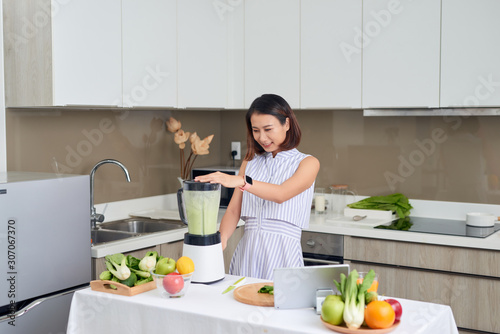 Beautiful Asian Woman juicing making green juice with juice machine in home kitchen. Healthy concept.