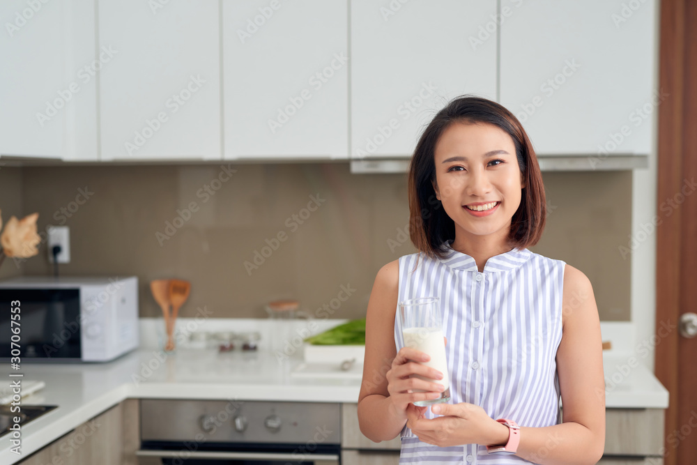 Beautiful young Asian woman drinking milk in the kitchen at home. Beautiful young Asian woman drinking milk in the kitchen at home.