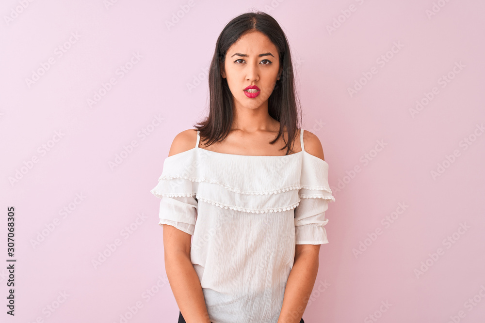 Beautiful chinese woman wearing white t-shirt standing over isolated pink background skeptic and nervous, disapproving expression on face with crossed arms. Negative person. Beautiful chinese woman wearing white t-shirt standing over isolated pink background skeptic and nervous, disapproving expression on face with crossed arms. Negative person.