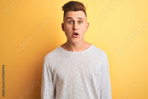 Young handsome man wearing white casual t-shirt standing over isolated yellow background afraid and shocked with surprise expression, fear and excited face.