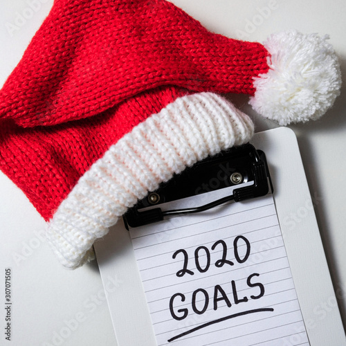 New year goals 2020 on desk. 2020 goals with notebook and red santa hat on white background. Resolutions, plan, strategy, change, idea concept