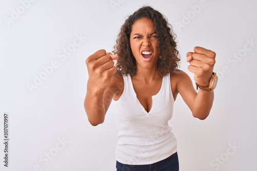 Fotografija Young brazilian woman wearing casual t-shirt standing over isolated white background angry and mad raising fists frustrated and furious while shouting with anger