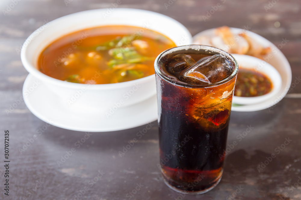 Pop water or cola in glass with ice cubes with food in the background. Pop water or cola in glass with ice cubes with food in the background.