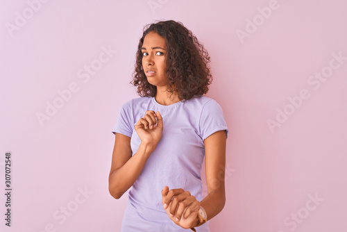 Young brazilian woman wearing t-shirt standing over isolated pink background disgusted expression, displeased and fearful doing disgust face because aversion reaction. With hands raised. Annoying 