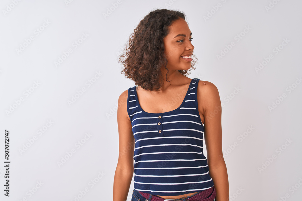 Young brazilian woman wearing striped t-shirt standing over isolated white background looking away to side with smile on face, natural expression. Laughing confident. Young brazilian woman wearing striped t-shirt standing over isolated white background looking away to side with smile on face, natural expression. Laughing confident.