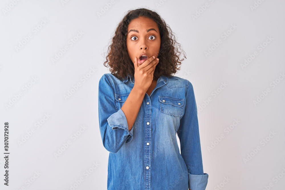Young brazilian woman wearing denim shirt standing over isolated white background Looking fascinated with disbelief, surprise and amazed expression with hands on chin Young brazilian woman wearing denim shirt standing over isolated white background Looking fascinated with disbelief, surprise and amazed expression with hands on chin