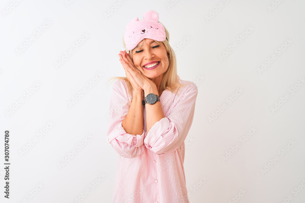 Middle age woman wearing sleep mask and pajama over isolated white background sleeping tired dreaming and posing with hands together while smiling with closed eyes. Middle age woman wearing sleep mask and pajama over isolated white background sleeping tired dreaming and posing with hands together while smiling with closed eyes.