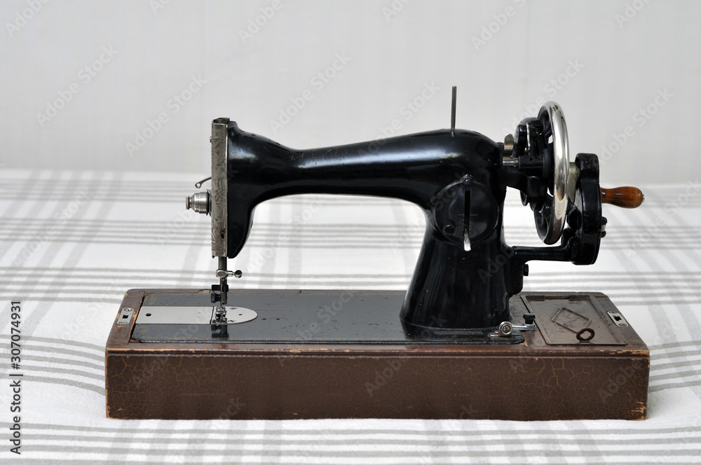 Vintage sewing machine with manual drive on the background of a linen tablecloth.