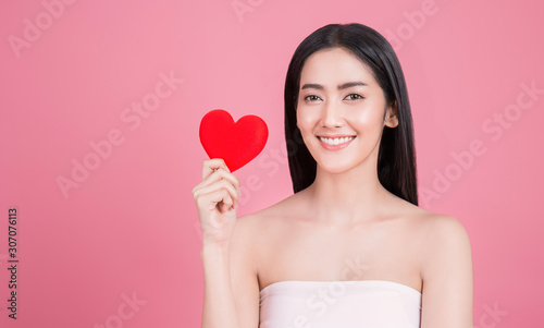 Portrait of young beautiful asian woman hands holding red heart shape isolated on pink background. Smiling Japanese girl face, love lifestyle valentines’ day. Beauty clinic spa concept photo