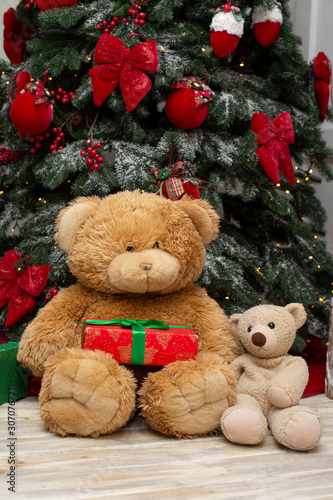 Two teddy bears with a Christmas present sitting near the Christmas tree.