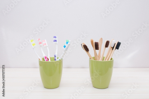plastic and bamboo toothbrushes in green cups, light background, copy space, eco friendly material concept