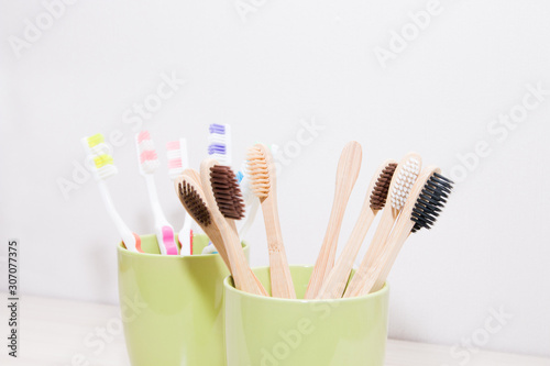 plastic and bamboo toothbrushes in green cups, light background, copy space, eco friendly Zero waste concept
