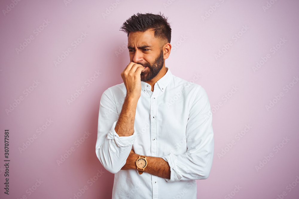 Young indian businessman wearing elegant shirt standing over isolated pink background looking stressed and nervous with hands on mouth biting nails. Anxiety problem. Young indian businessman wearing elegant shirt standing over isolated pink background looking stressed and nervous with hands on mouth biting nails. Anxiety problem.