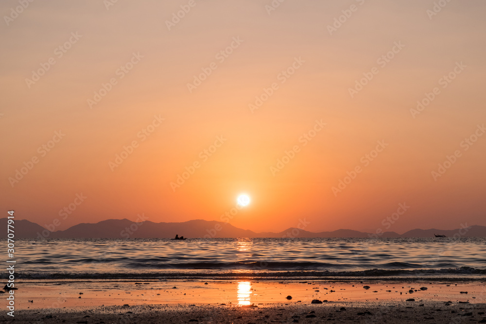 Beautiful evening seascape. Sunset and mountains on the horizon. The sun is reflected in the sea. Lonely boats are floating.
