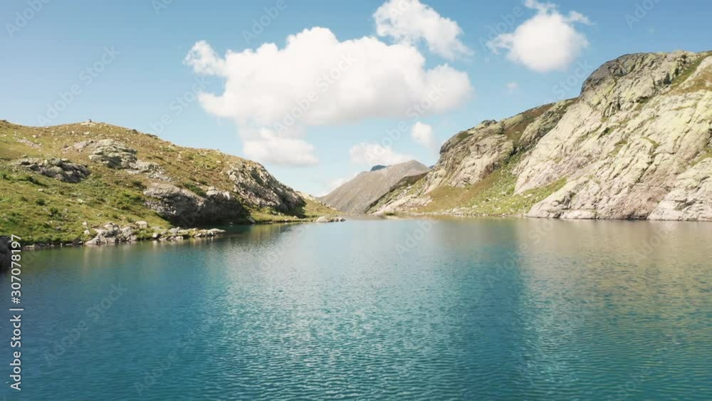 Aerial view; drone flies over glassy surface of mountain lake surrounded of stones, rocks; reflection of blue cloudy sky in sunny day; turquoise crystal clear water of highland glacier pond, Caucasus Aerial view; drone flies over glassy surface of mountain lake surrounded of stones, rocks; reflection of blue cloudy sky in sunny day; turquoise crystal clear water of highland glacier pond, Caucasus