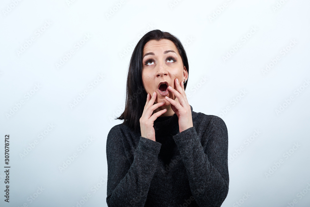 Shocked caucasian young woman in fashion black sweater over isolated white background, keeping hand on face with opened mouth, looking up. Lifestyle concept Shocked caucasian young woman in fashion black sweater over isolated white background, keeping hand on face with opened mouth, looking up. Lifestyle concept