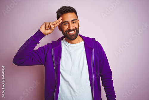 Young indian man wearing purple sweatshirt standing over isolated pink background Smiling pointing to head with one finger, great idea or thought, good memory © Krakenimages.com