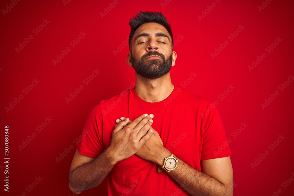 Φωτογραφία Young handsome indian man wearing t-shirt over isolated red background smiling with hands on chest with closed eyes and grateful gesture on face