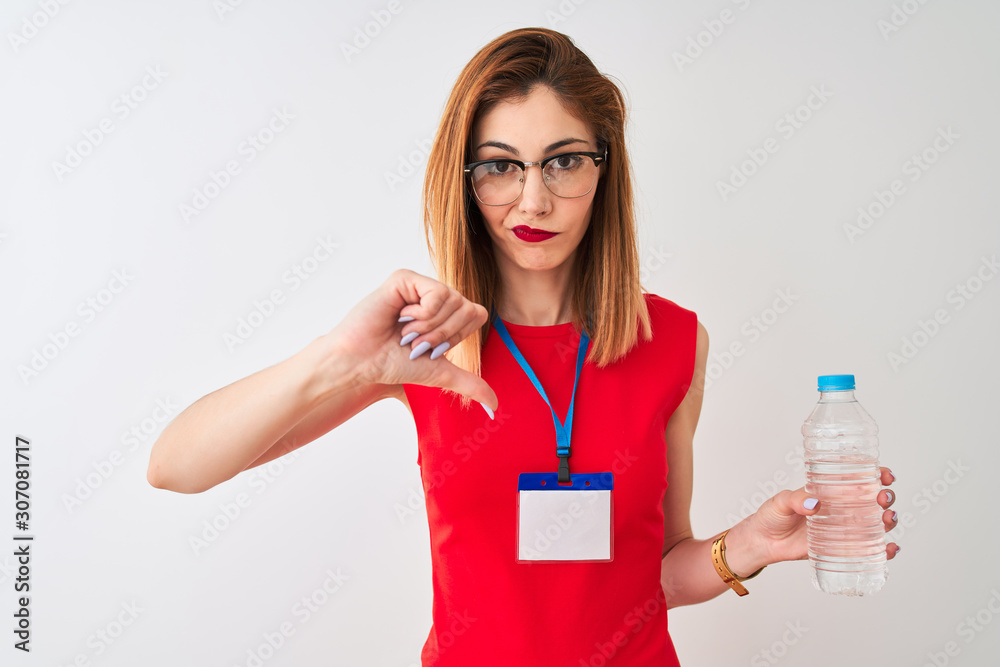 Redhead businesswoman wearing id card drinking water over isolated white background with angry face, negative sign showing dislike with thumbs down, rejection concept Redhead businesswoman wearing id card drinking water over isolated white background with angry face, negative sign showing dislike with thumbs down, rejection concept