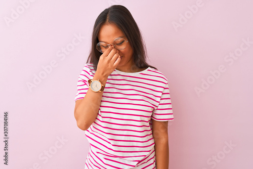 Young chinese woman wearing striped t-shirt and glasses over isolated pink background tired rubbing nose and eyes feeling fatigue and headache. Stress and frustration concept.