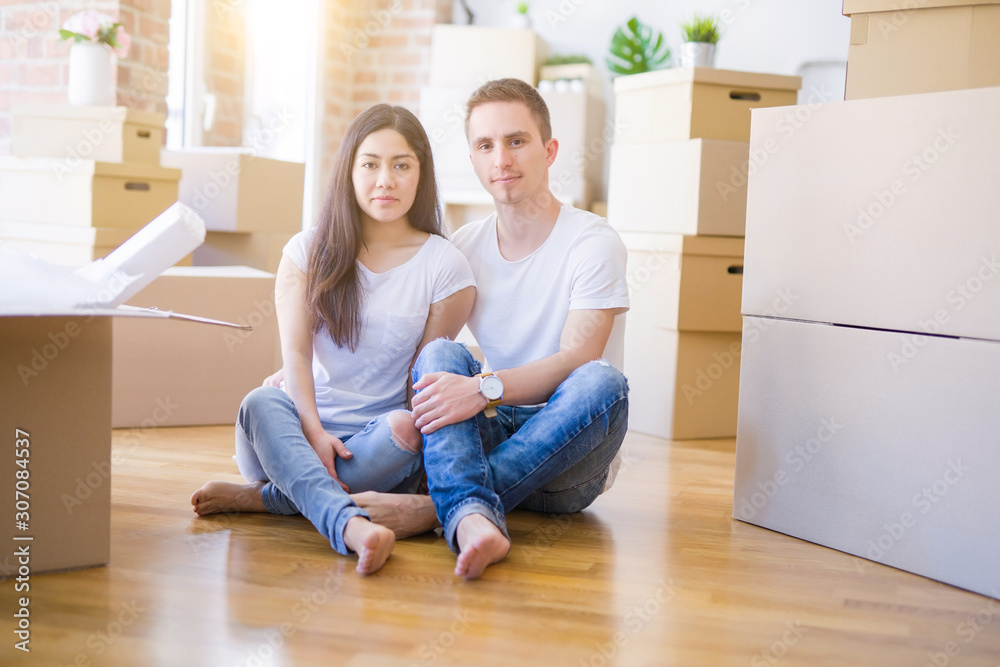 Young beautiful couple sitting on the floor at new home around cardboard boxes with a confident expression on smart face thinking serious Young beautiful couple sitting on the floor at new home around cardboard boxes with a confident expression on smart face thinking serious