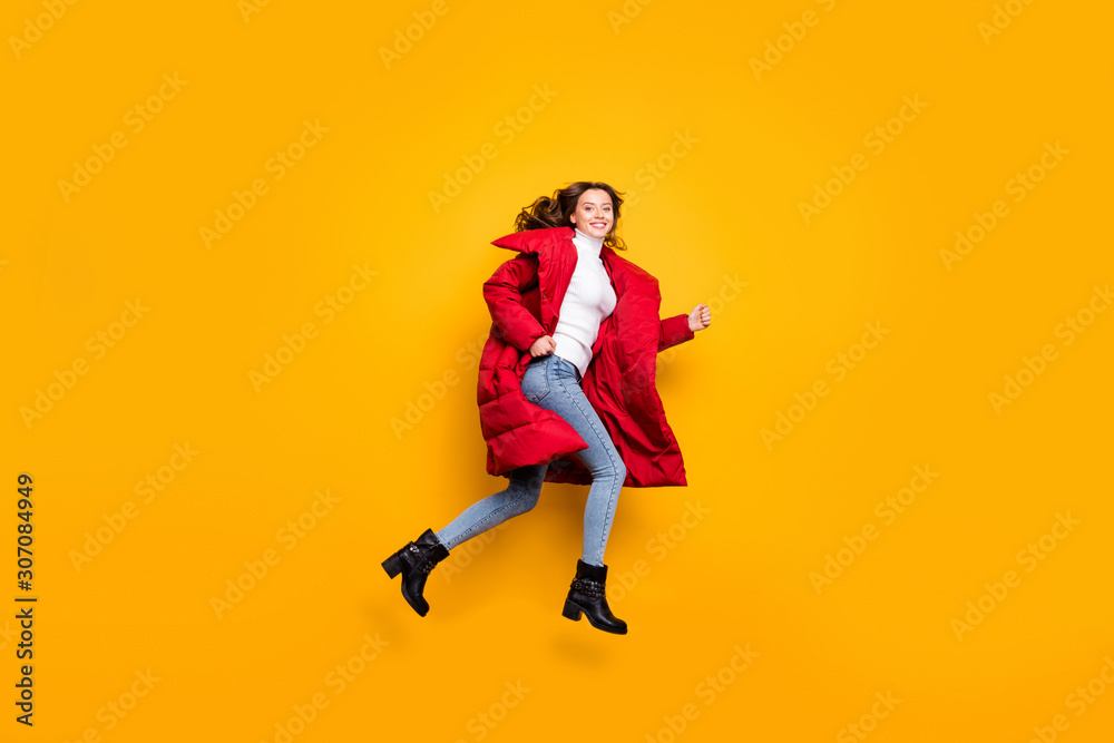 Full length photo of charming lady jumping high sunny fall day rushing shopping wear jeans shoes white pullover red long winter coat isolated yellow color background
