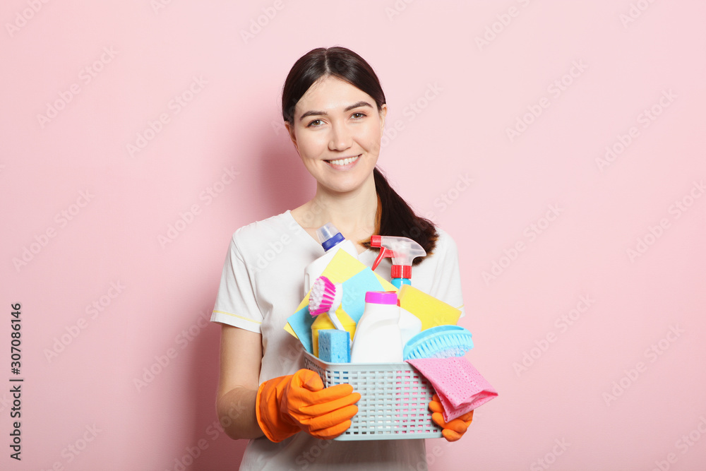 A young housewife holds in his hands cleaning products on a colored background. A young housewife holds in his hands cleaning products on a colored background.