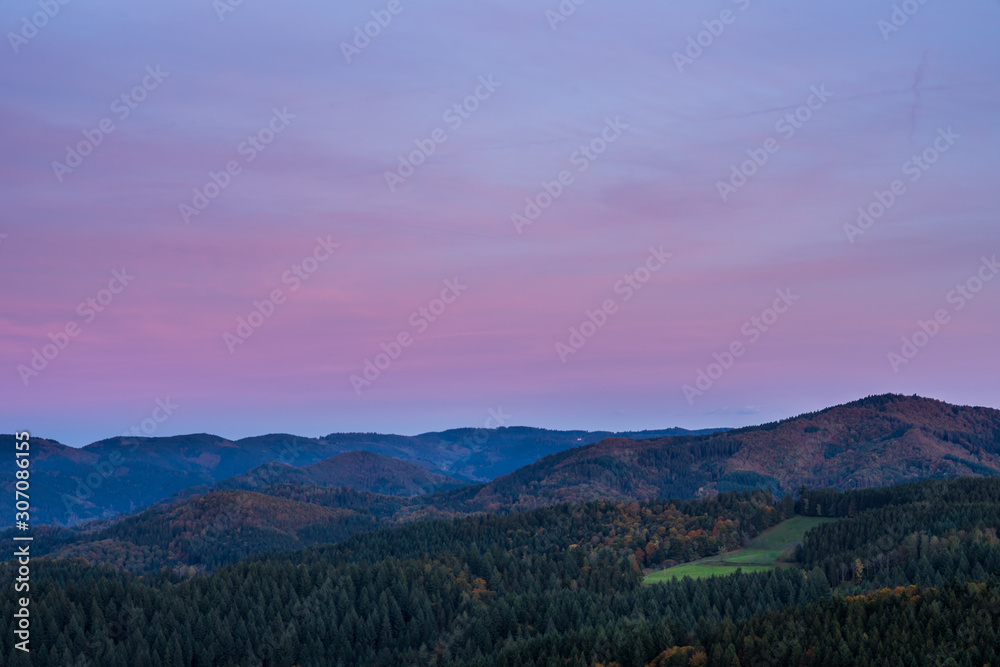 Germany, Wide beautiful untouched black forest nature landscape of forest covered hills and mountains under red glowing sky after sunset, aerial view above