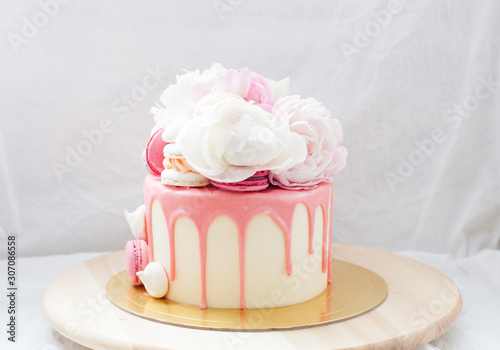 White cake with pink melted chocolate, fresh roses and peonies, macaroons and meringues. 
