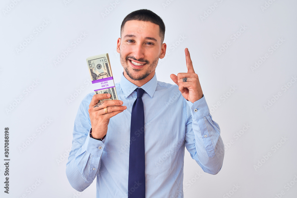 Young handsome business man holding a bunch of dollars bank notes over isolated background surprised with an idea or question pointing finger with happy face, number one Young handsome business man holding a bunch of dollars bank notes over isolated background surprised with an idea or question pointing finger with happy face, number one
