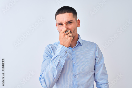 Young handsome business man standing over isolated background smelling something stinky and disgusting, intolerable smell, holding breath with fingers on nose. Bad smells concept.