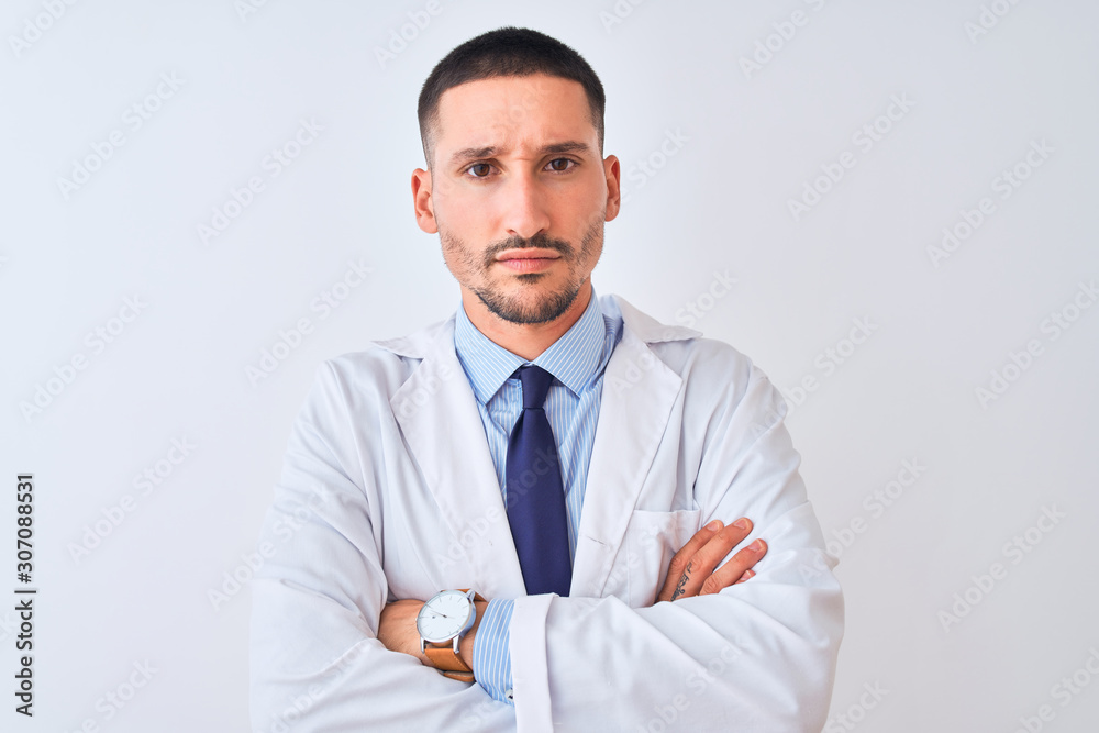Young doctor man wearing white coat over isolated background skeptic and nervous, disapproving expression on face with crossed arms. Negative person. Young doctor man wearing white coat over isolated background skeptic and nervous, disapproving expression on face with crossed arms. Negative person.