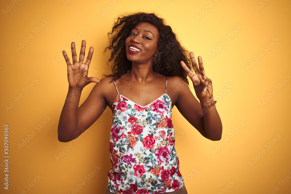 African american woman wearing floral summer t-shirt over isolated yellow background showing and pointing up with fingers number eight while smiling confident and happy. African american woman wearing floral summer t-shirt over isolated yellow background showing and pointing up with fingers number eight while smiling confident and happy.