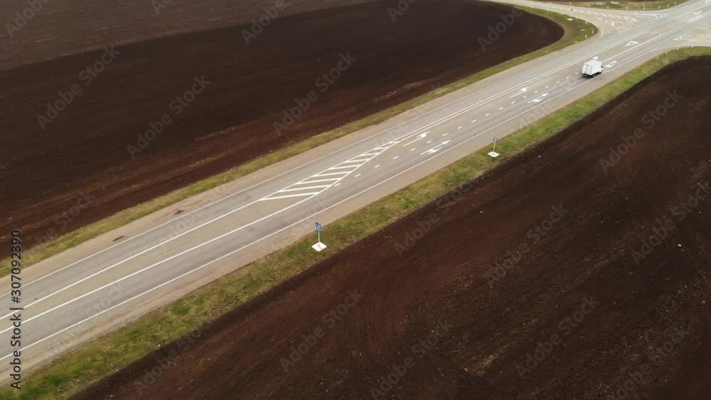 Aerial view of a rural asphalt motorway. Cars are moving along the highway. Cars and trucks drive along a country road. Highway road air footage. Plowed fields around the road Aerial view of a rural asphalt motorway. Cars are moving along the highway. Cars and trucks drive along a country road. Highway road air footage. Plowed fields around the road