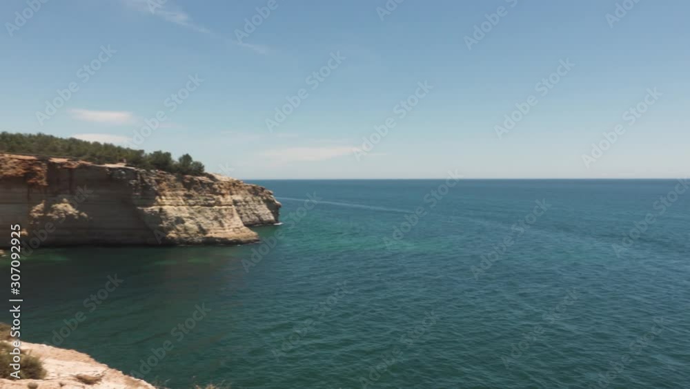 pan right in portugal on algave coast blue sky and clear sea or ocean with cliffside very little clouds pan right in portugal on algave coast blue sky and clear sea or ocean with cliffside very little clouds