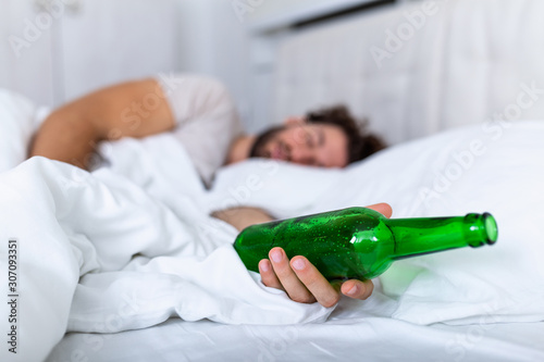 Unconscious drunk man with bottle of alcohol in hands sleeping in bed . Alcoholism problem and hangover concept photo