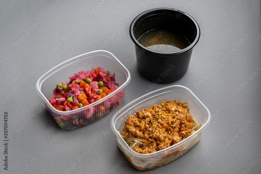 Pasta with minced meat and onion in navy-style and a jar of vinaigrette on a gray background. Food from delivery. Pasta with minced meat and onion in navy-style and a jar of vinaigrette on a gray background. Food from delivery.