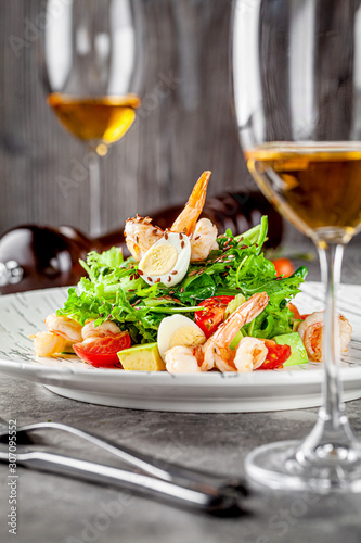 Caesar salad with seafood and shrimp. A glass of white wine on the table. Modern serve in a restaurant. Background image. Copy space.